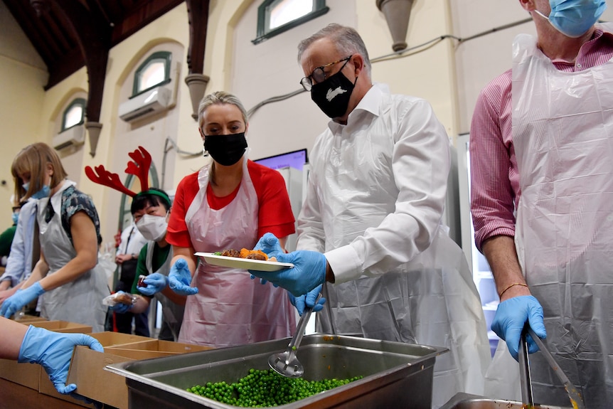 Jodie Haydon and Anthony Albanese prepare plates of Christmas lunch wearing face masks and gloves