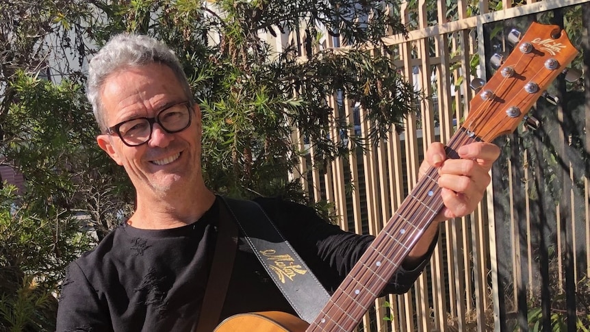 A man with grey hair and a guitar.