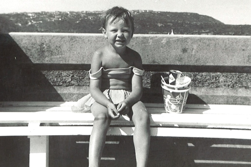 A black and white photo of a young girl sitting on a bench. 