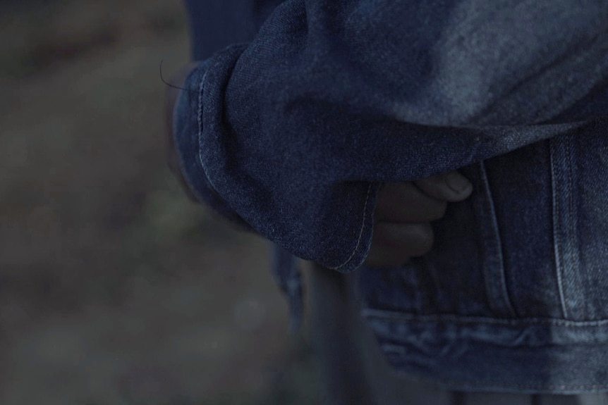 A person's hands crossed over inside the sleeves of a denim jacket. 