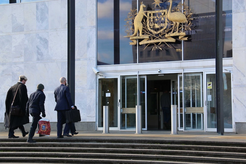 David Eastman carries an Aldi bag as he walks into the ACT Supreme Court, flanked by lawyers.