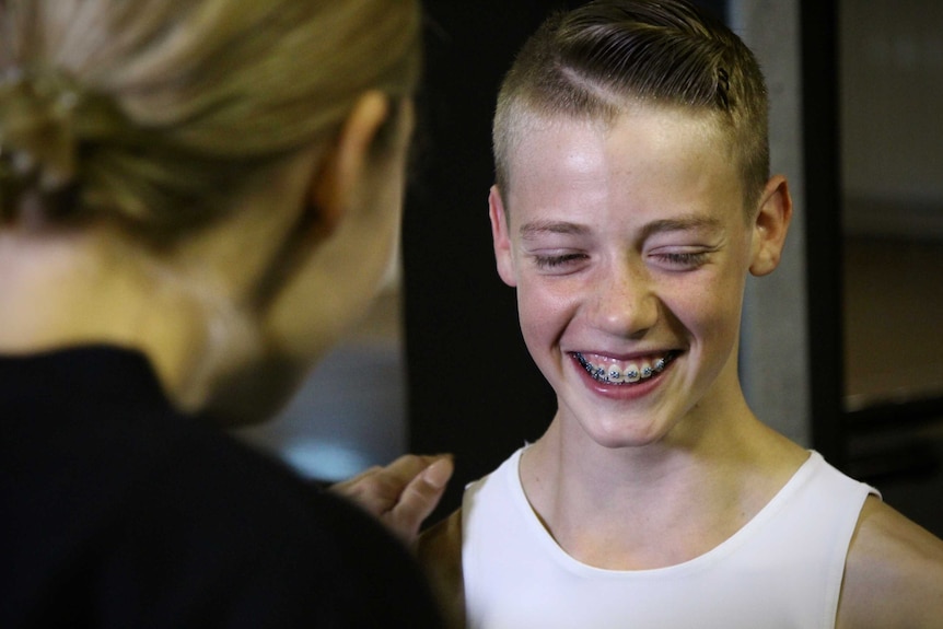 A boy in a ballet uniform smiles