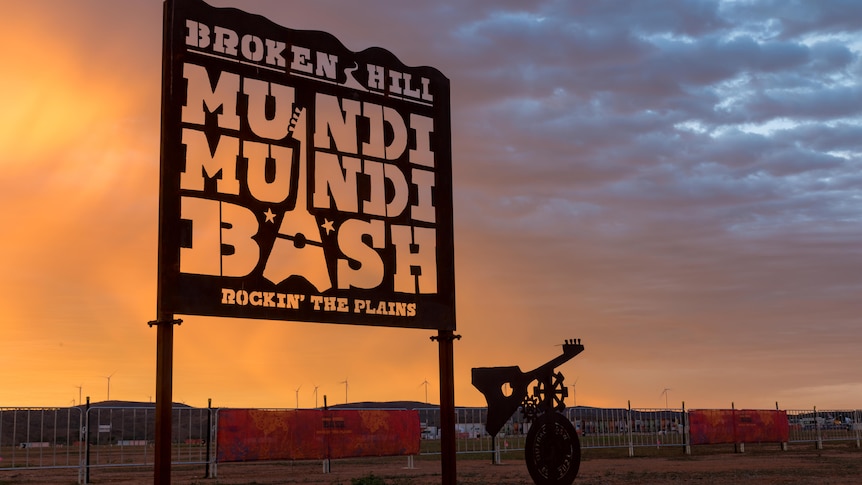 A sign that says Broken Hill Mundi Mundi Bash Rockin The Plains in front of a sunset