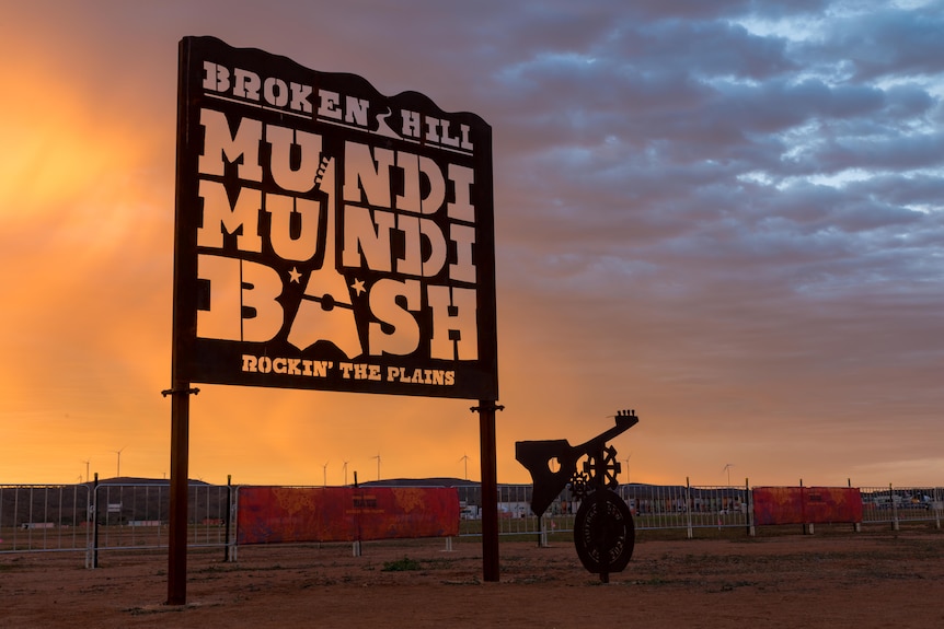 A sign that says Broken Hill Mundi Mundi Bash Rockin The Plains in front of a sunset