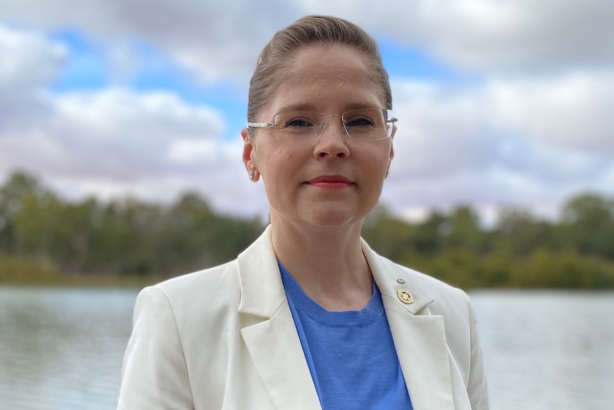 A woman is standing looking at the camera with the river behind her.