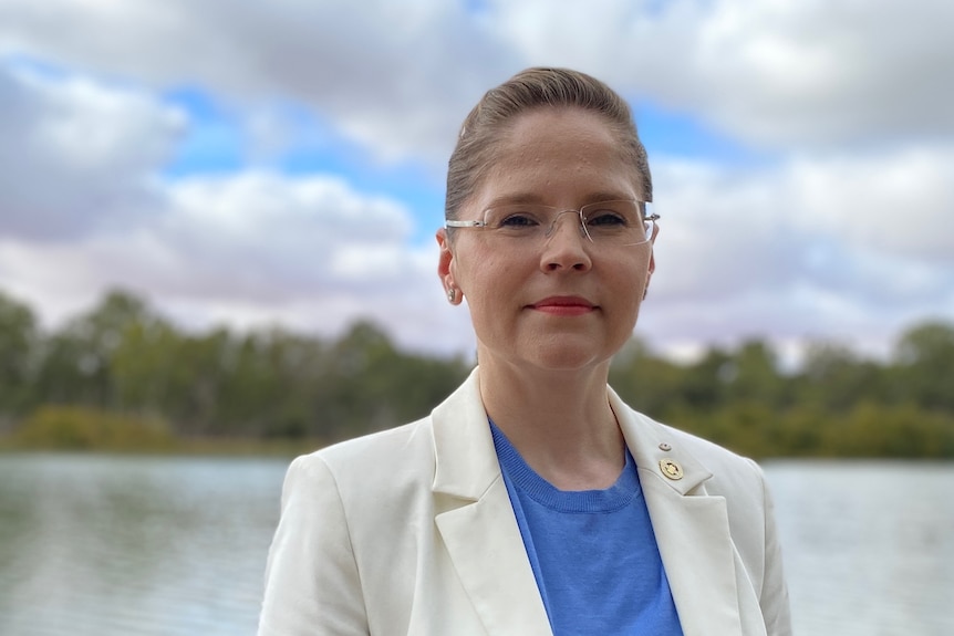 A woman is standing looking at the camera with the river behind her.