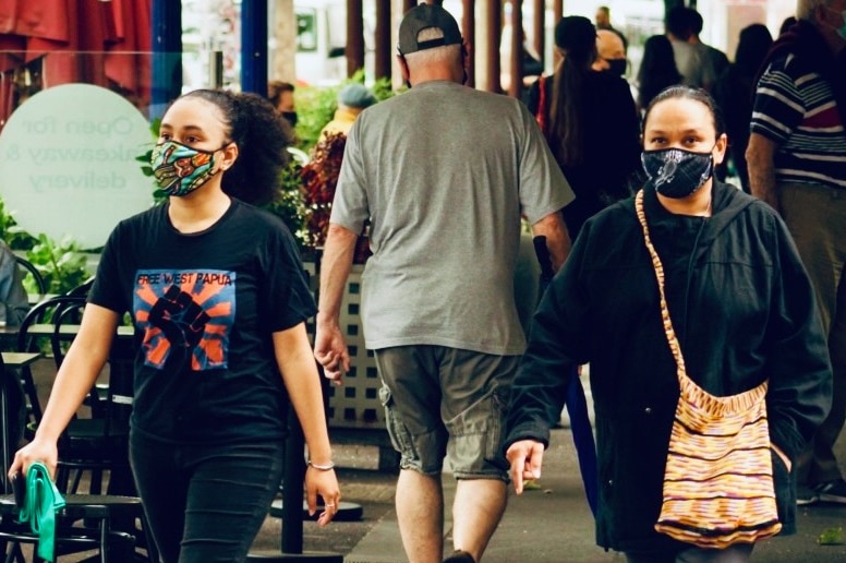 Two women wearing black masks with patterns walk by a cafe.