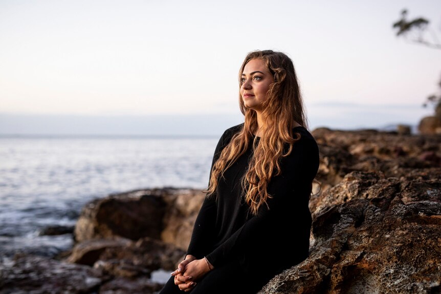 young woman stares out to sea on a coastline in southern lutruwita/Tasmania
