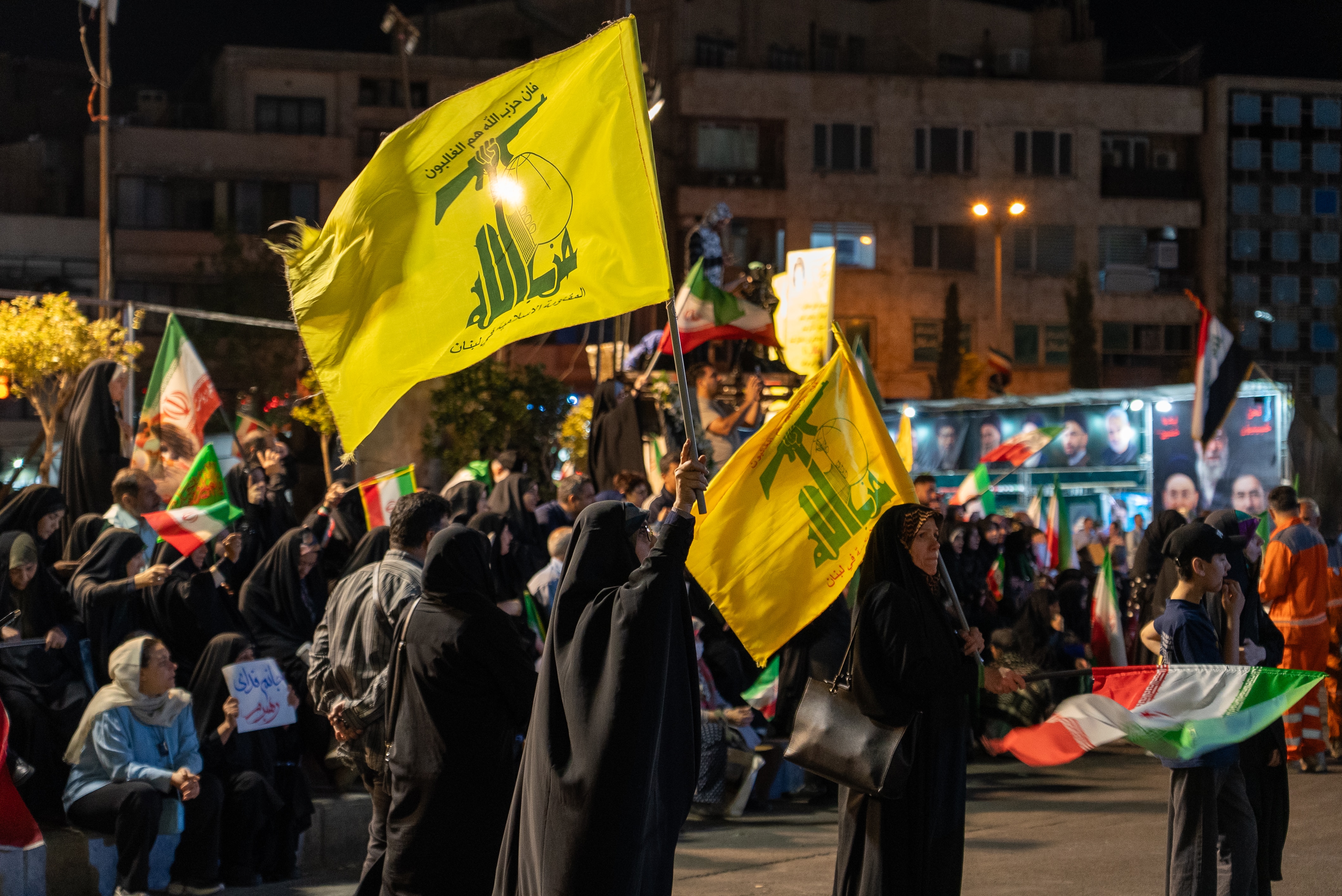 Women in traditional Islamic attire waving a yellow Hezbollah flag.