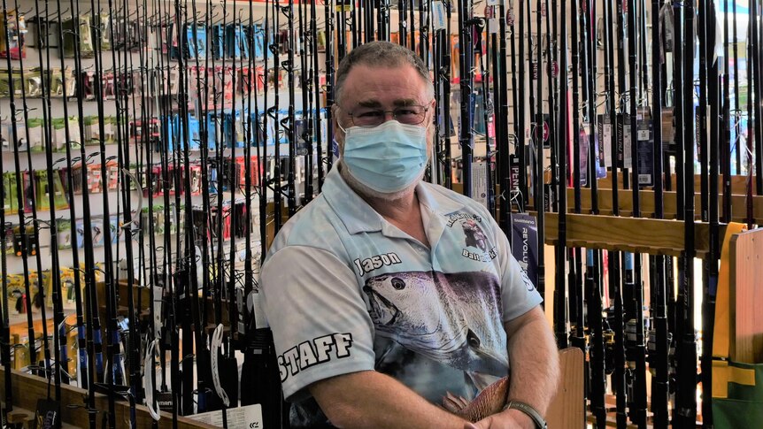 Man in blue mask stands in front of fishing rods. 