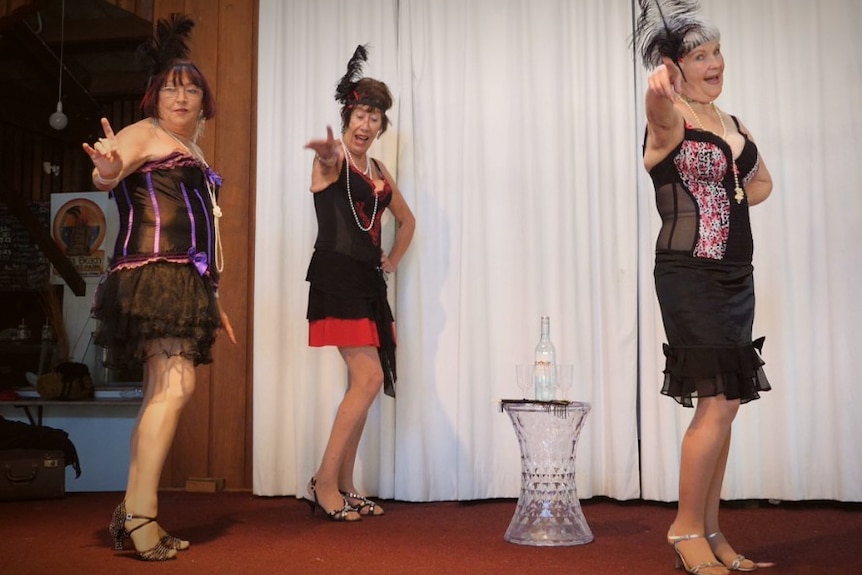 Four women standing on a stage in skimpy and sassy dresses, feather head dress heals and sparkles