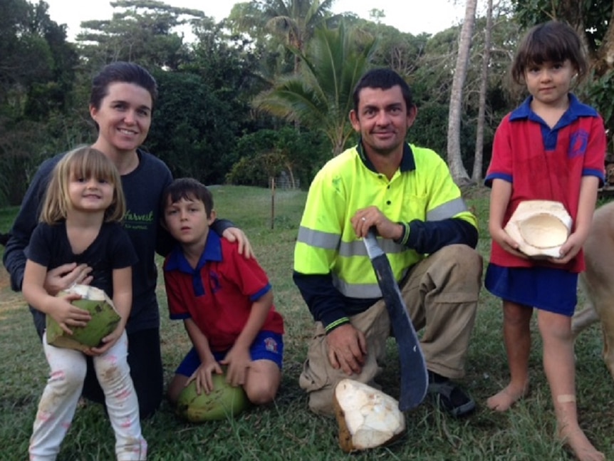 The Willetts family kneeling on the ground holding coconuts and a machete used to open them