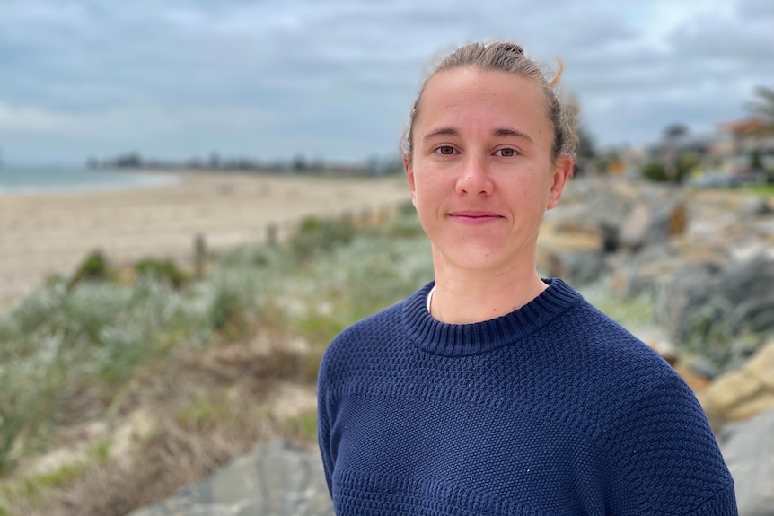 A woman stands on the shore of a beach.