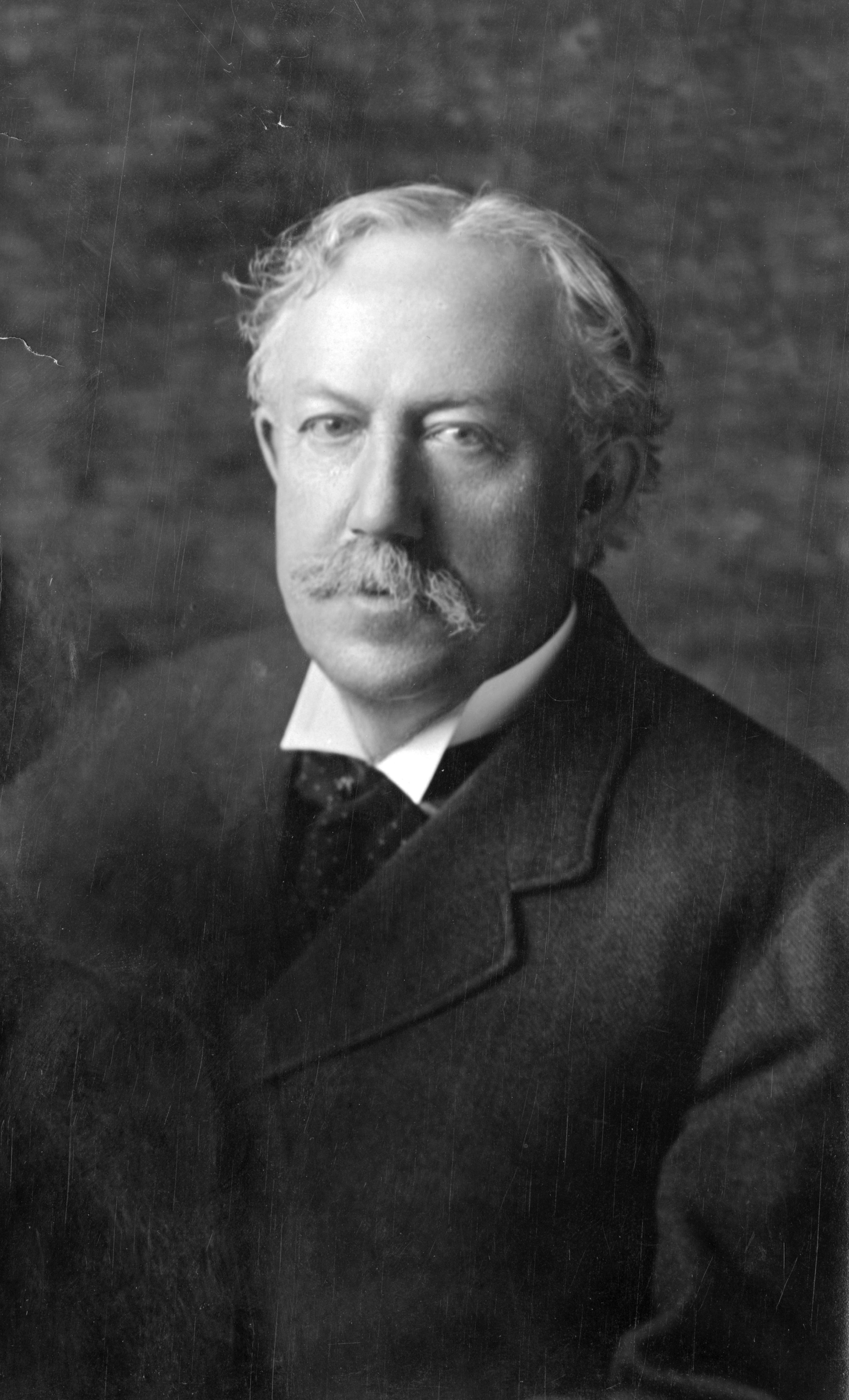 An old black and white photo of an older man with white hair and a moustache