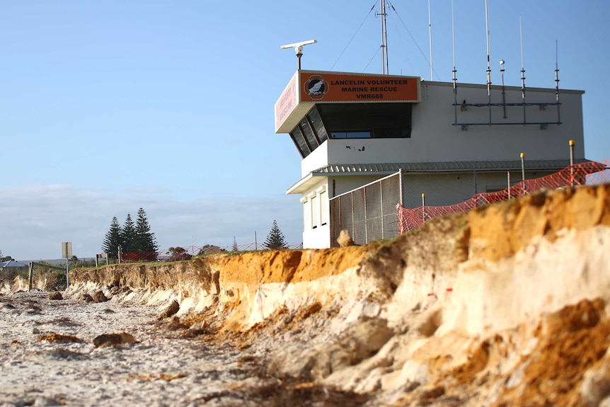 A tall building stands above a badly eroded stretch of beach.