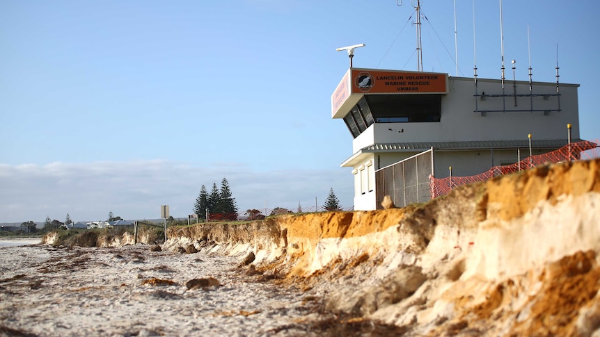 A tall building stands above a badly eroded stretch of beach.