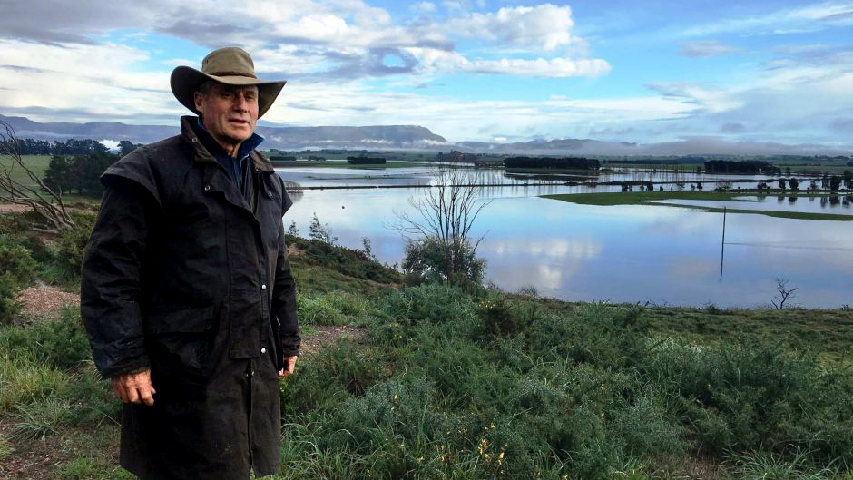 Farmer George Mills stands in front of a flooded paddock