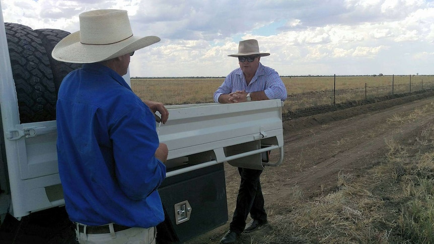 Tony Rayner leans against the back of a white ute facing grazier David Fysh. The dog fence is in the background.