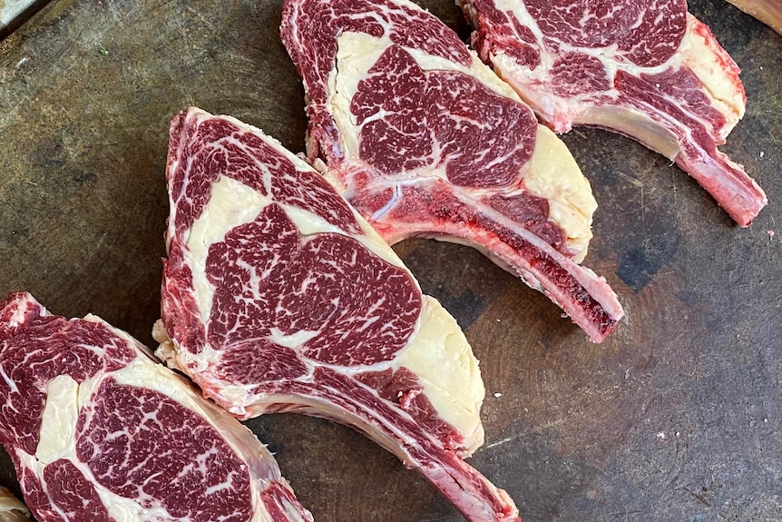 A group of heavily marbled steaks lay on a cutting board. 