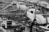 A black and white photo shows rows of Volkswagen Beetle chassis assembly lines.