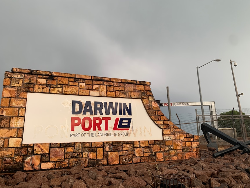 A black, red and white sign saying Darwin Port attached to a stone wall.