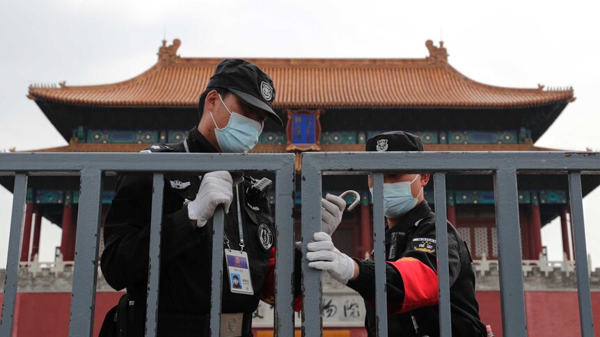 Two guards lock a gate in front of a building in China.