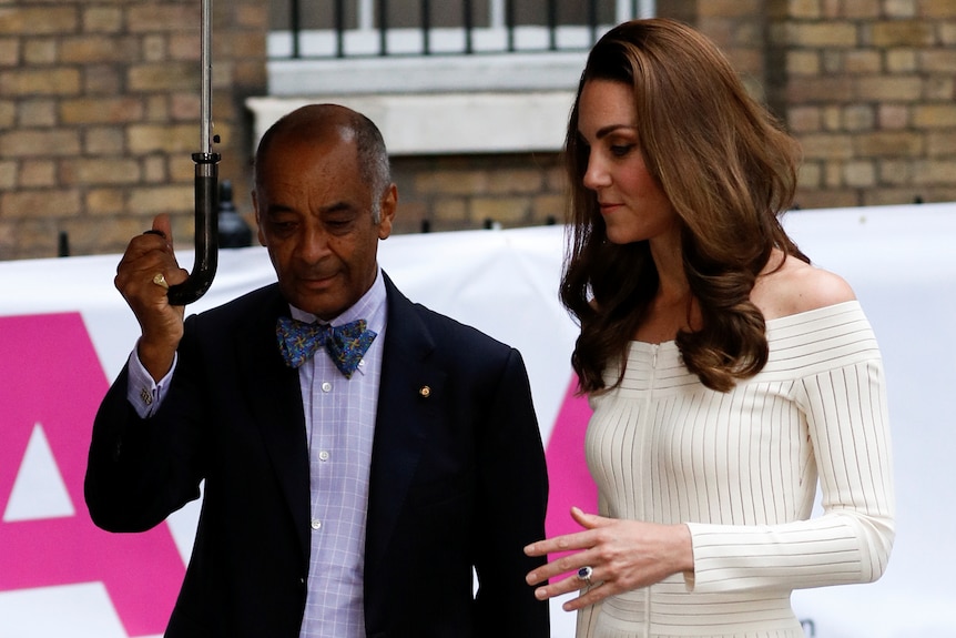 Kenneth Olisa holds up an umbrella as he walks side by side with the Duchess of Cambridge