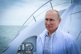 Vladimir Putin in a white member's only jacket standing on a yacht, with a slight smile on his face