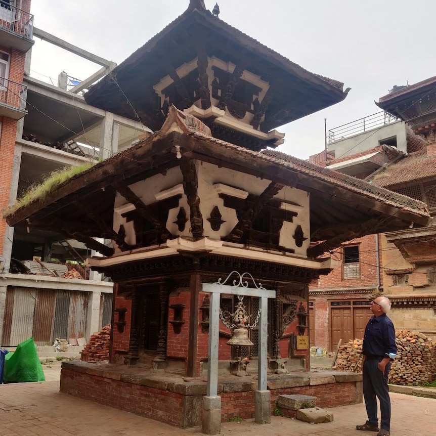 Kanak Mani Dixit stands in a dark blue shirt outside the temple and looks up at it.