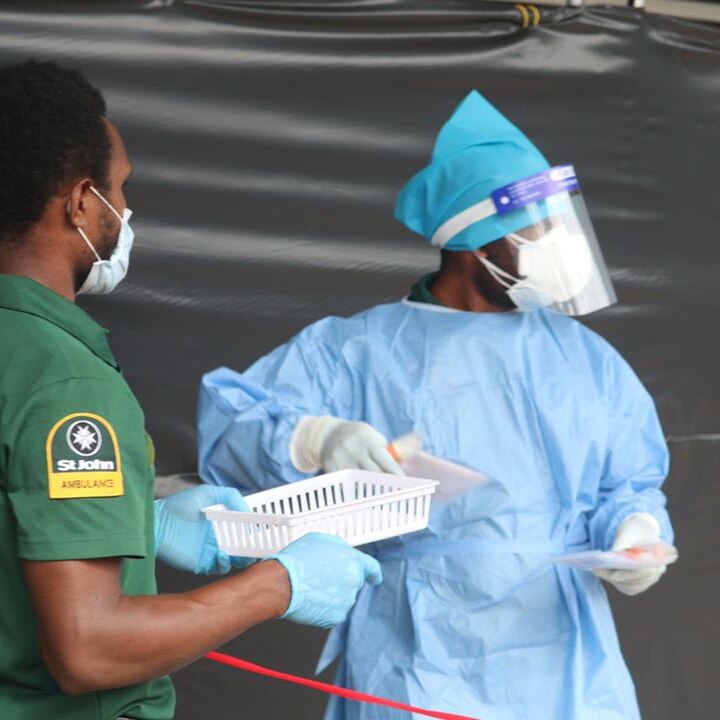 Two medical workers wearing masks stand in the street.