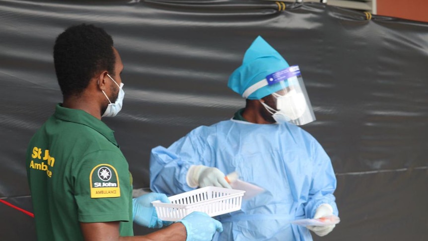 Two medical workers wearing masks stand in the street.