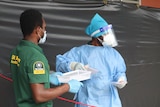 Two medical workers wearing masks stand in the street.