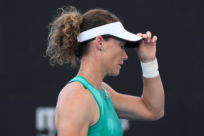 Sam Stosur closes her eyes and holds the end of the peak on her white visor