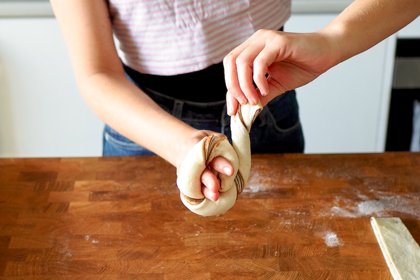 Strips of the dough are twisted on one hand to form the knot shape before baking.