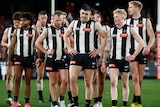 Collingwood players stand in a line and look down