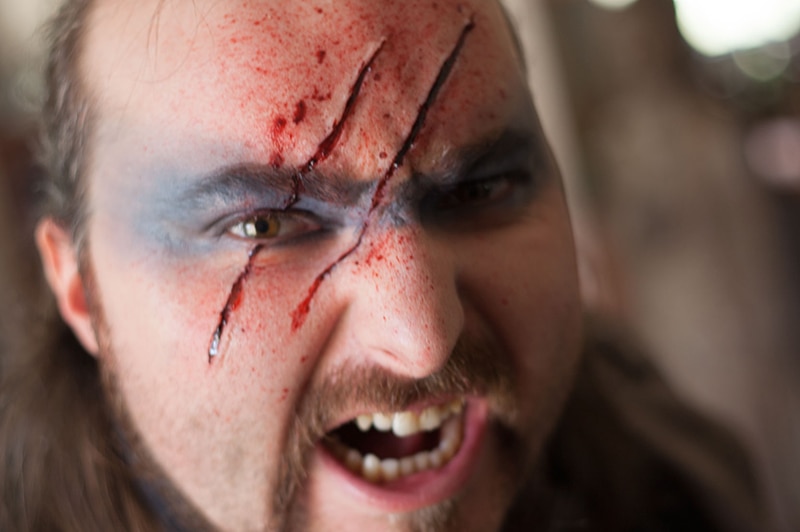 A man with theatre makeup and two large (fake) claw marks slashed across his face snarls at the camera.