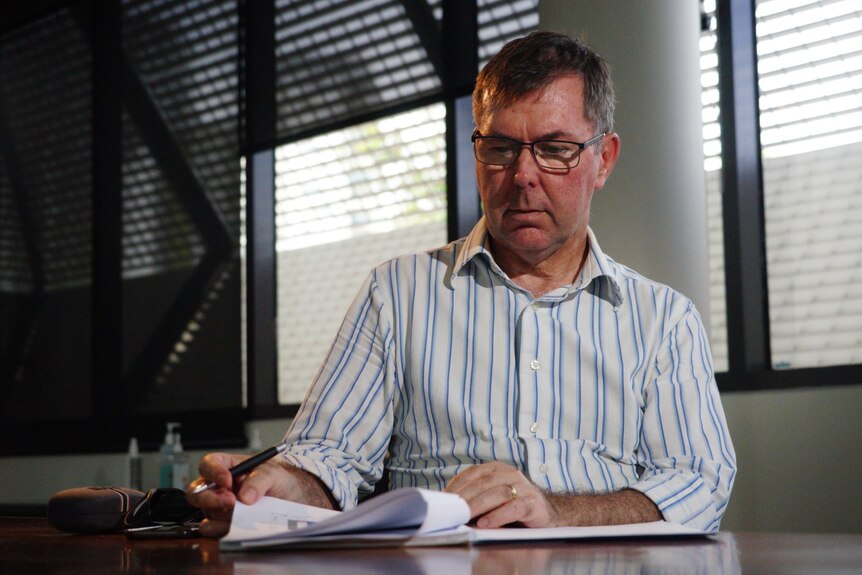 A man sitting in a boardroom looks down at some documents with a slight look of concern.
