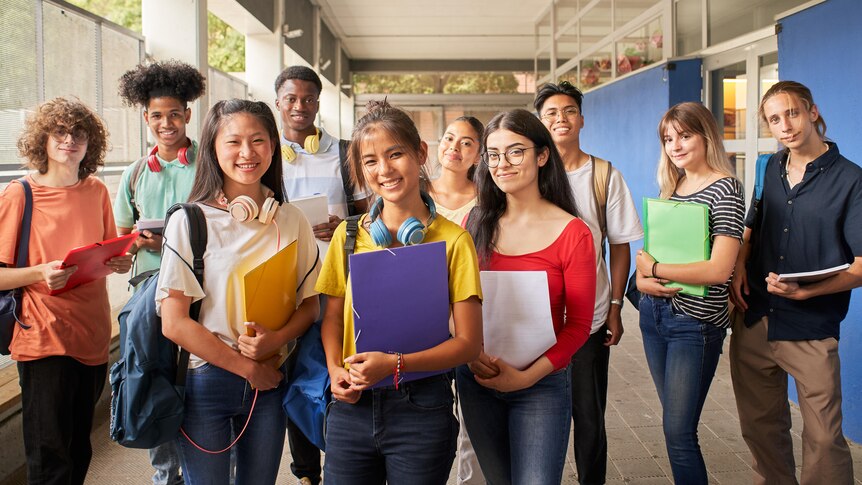 Ten diverse high school students in plain clothes standing in a school corridor.