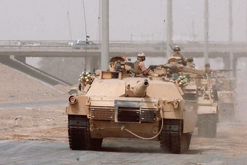US tanks driving in front of a sign that points to Fallujah, in Iraq.