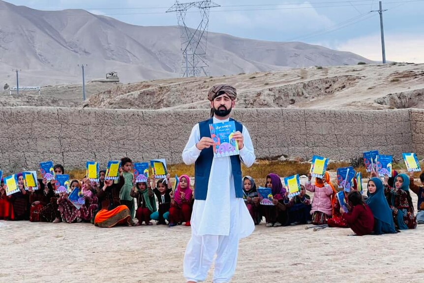 Matiullah Wesa holds up a book in front of a group of girls holding up books.