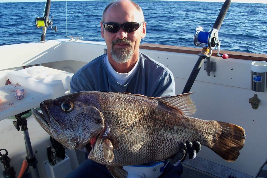 A man on a boat holding a large fish