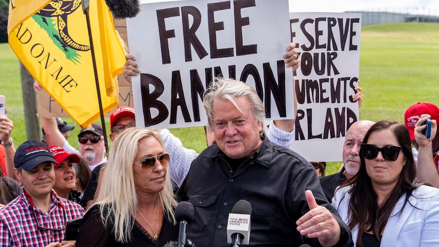 Man talks into microphone, banners behind read 'free bannon'