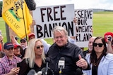 Man talks into microphone, banners behind read 'free bannon'