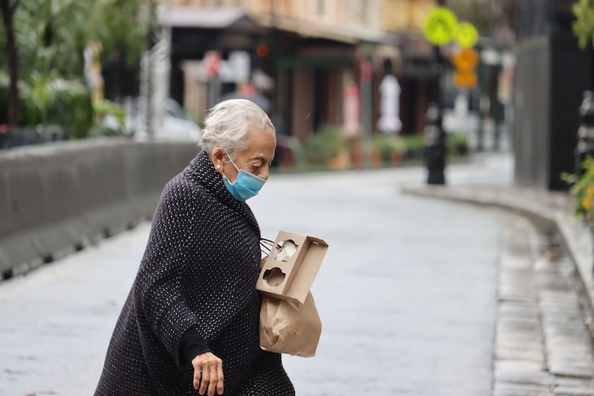 Woman wearing mask crosses empty street.