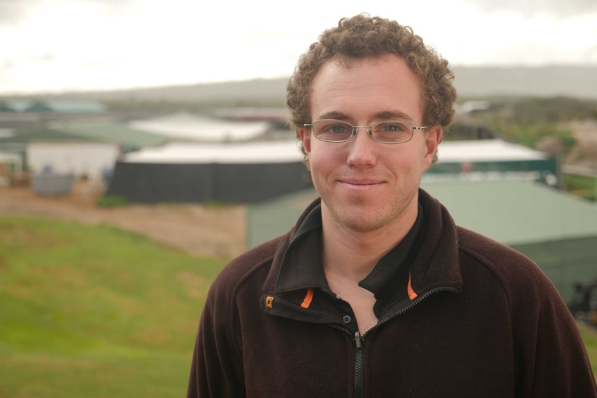 Jake Poad stands on the coast with an abalone farm in the background.