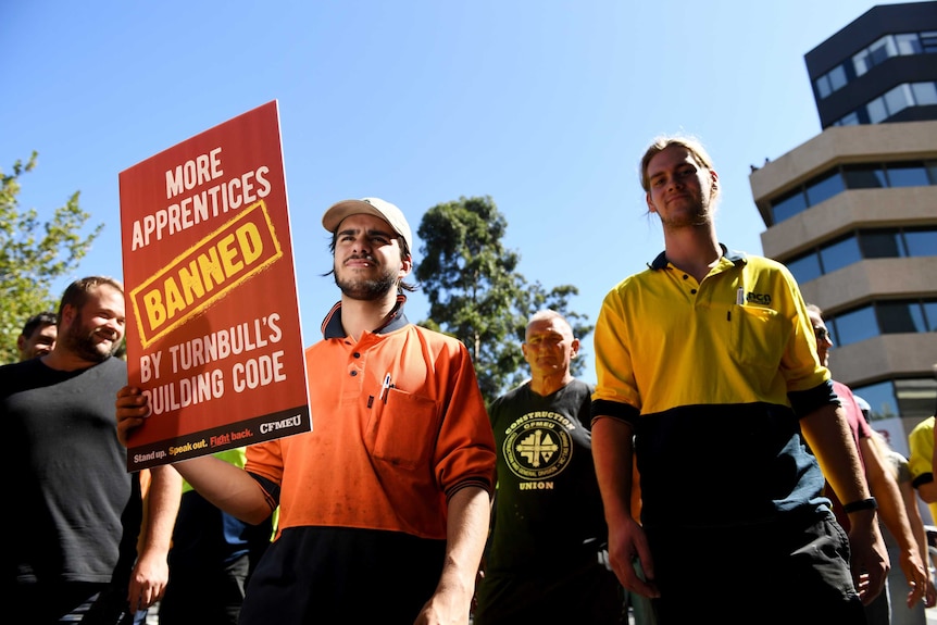 A man holds a sign that says 'More apprentices banned by Turnbull's building code'.