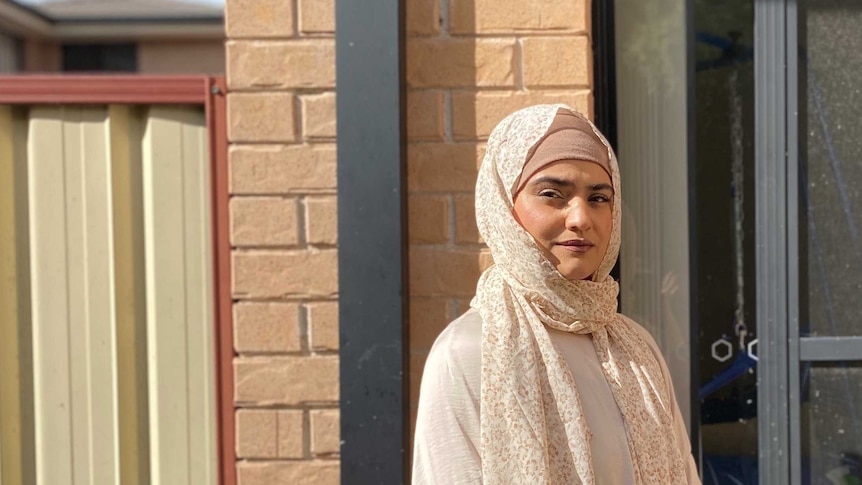 Nasreen Hanifi 戴着头巾，站在她家外面，背景是砖块。