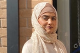 Nasreen Hanifi wearing hijab, standing outside of her house, bricks in background.
