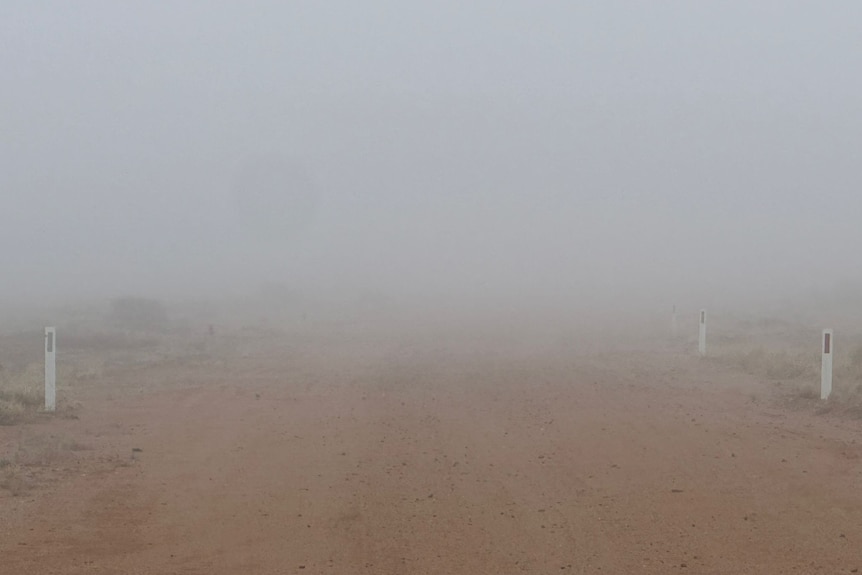An outback dirt road is barely visible through a blanket of thick fog. 