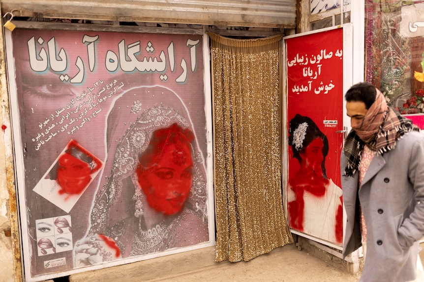 A man walks past a beauty shop with defaced pictures of women in Kabul